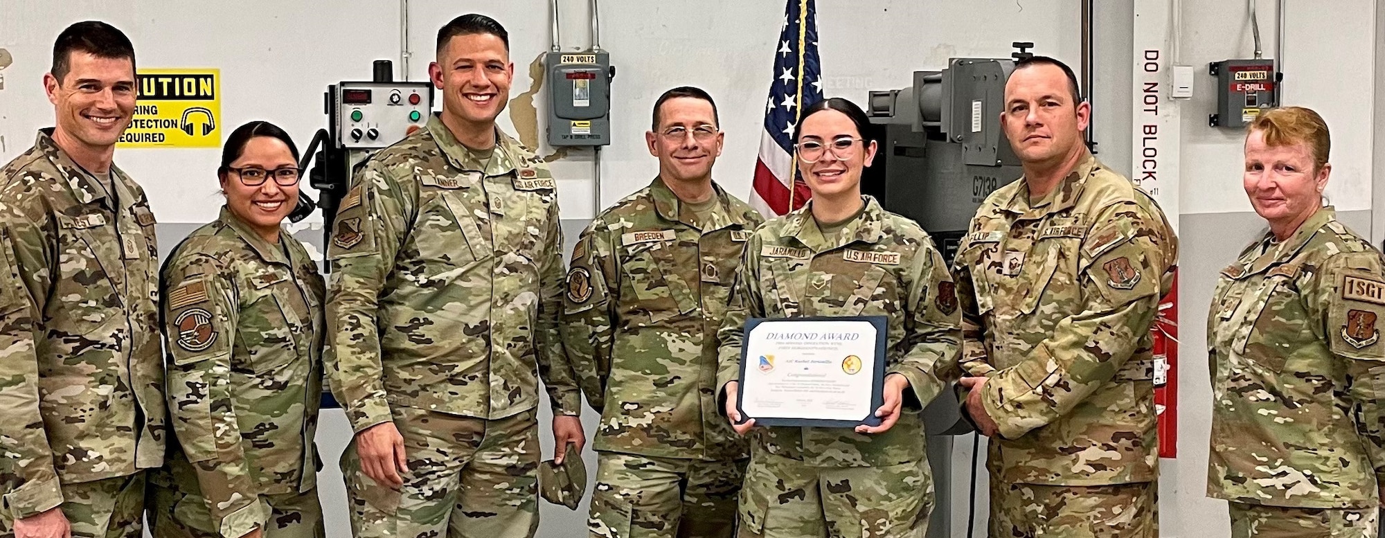 A female in uniform is receiving an award from of group of uniformed personnel.