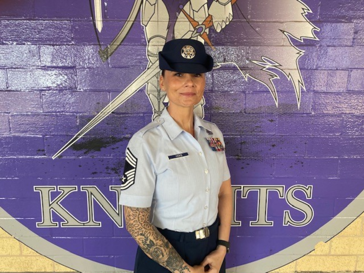 CMSgt Nicole Hicks stands in front of the logo for the 324th TRS.