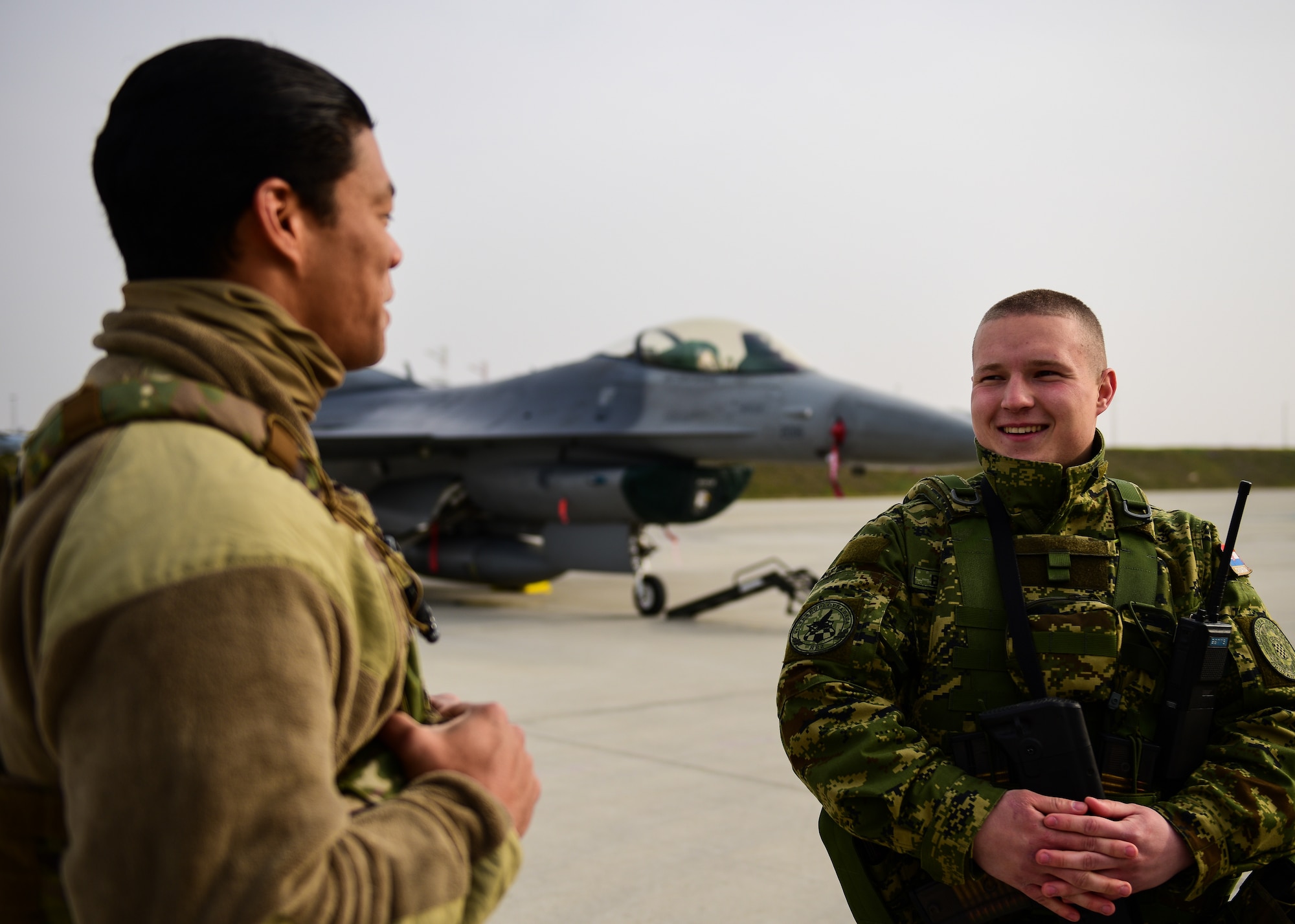 U.S. Air Force Staff Sgt. James Donaldson, 31st Security Forces Squadron response team leader, from the 31st Fighter Wing, Aviano Air Base, Italy, engages in conversation with Croatian Air Force Soldier Din Begulic, 191st Ela-Fighter Jet Unit while standing guard in front of a U.S. Air Force F-16C Fighting Falcon, while it receives routine maintenance for Agile Combat Employment operations at Croatia’s 91st Air Base at Pleso, March 17, 2022. The 31st FW executed ACE operations with Croatian Allies. Missions such as these enhance the readiness necessary to respond to any potential challenge in Southeast Europe. (U.S. Air Force photo by Tech. Sgt. Miquel Jordan)