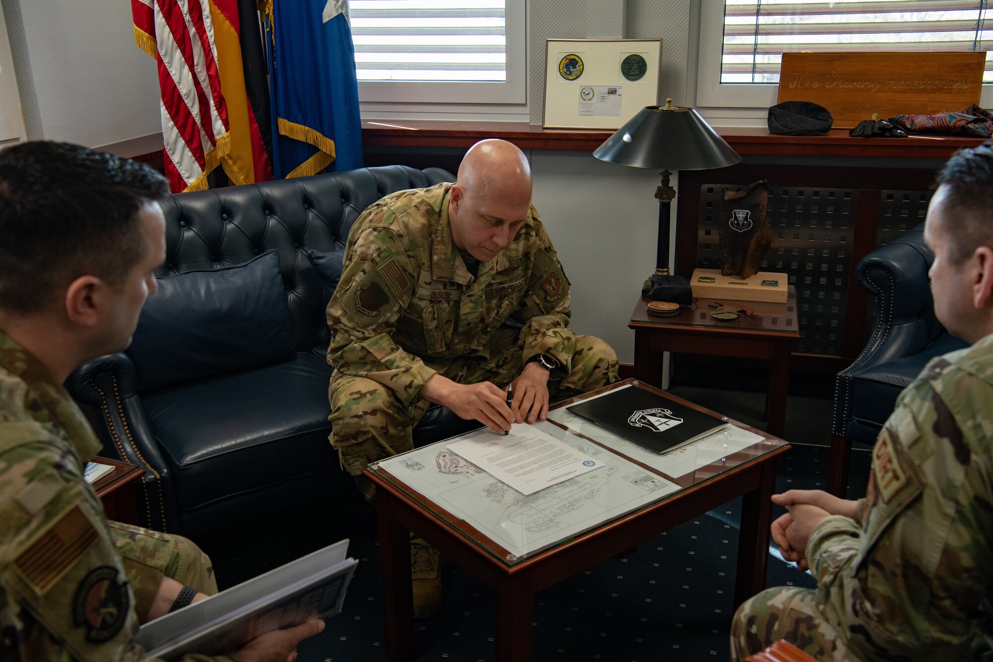 Three men sit in chairs, one man looks over document