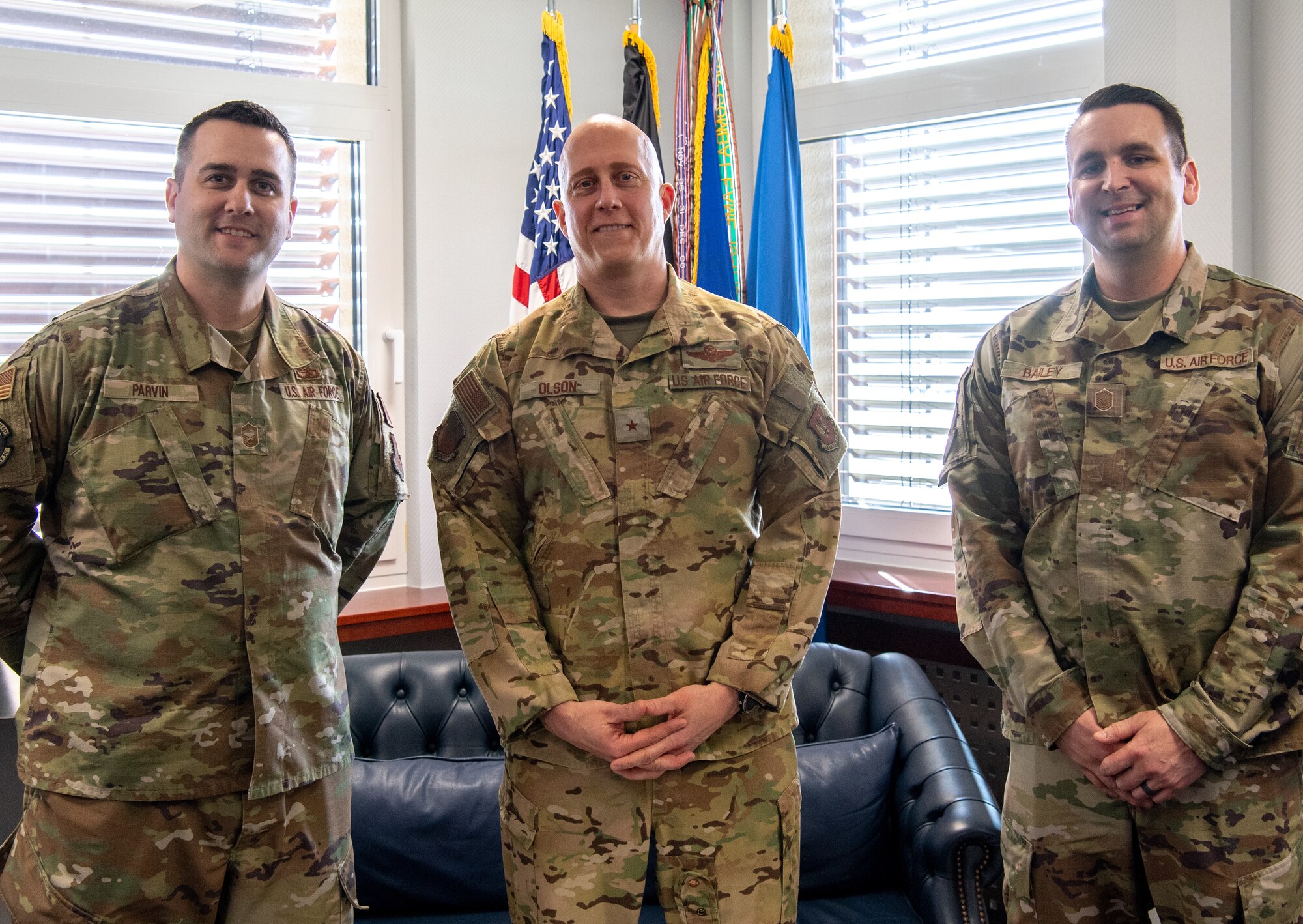 Three men stand together in front of flags