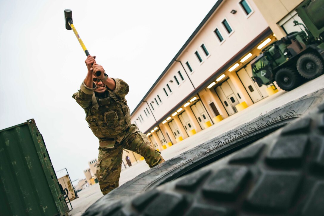 A soldier uses a sledgehammer to hit a tractor tire.