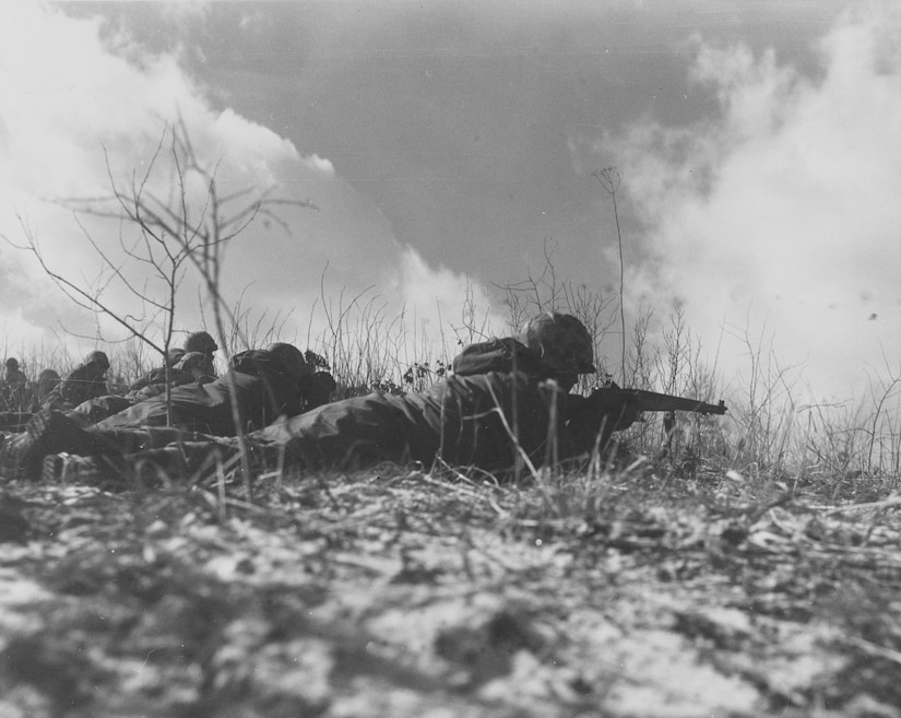 Several men lie in prone position on the ground while aiming their rifles.