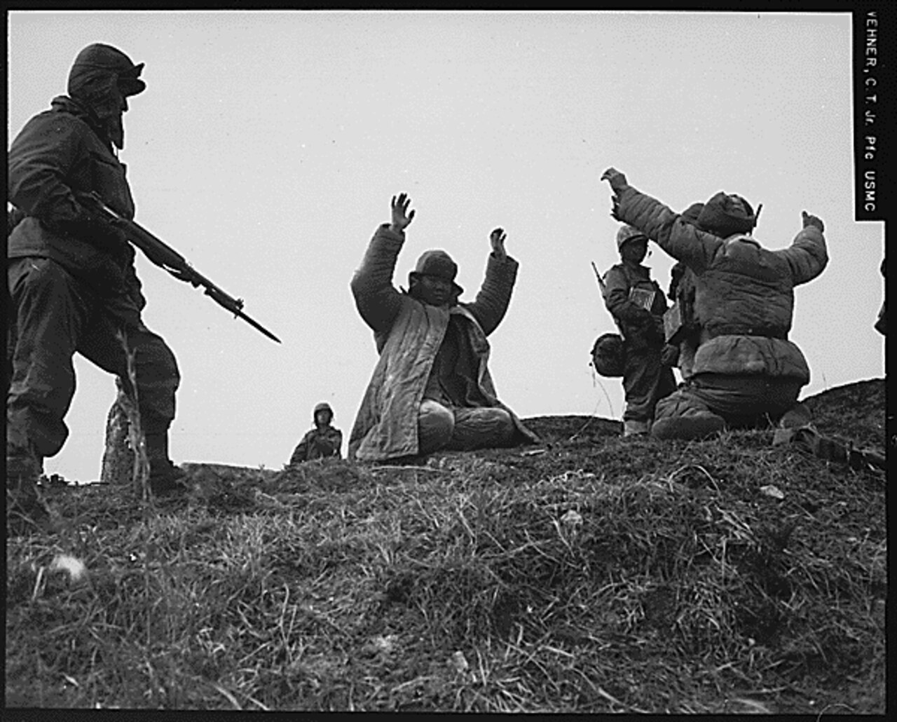A man points a rifle at two other men who have their hands up.
