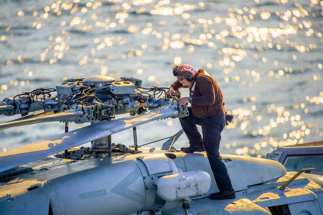 A sailor works on a helicopter rotor.