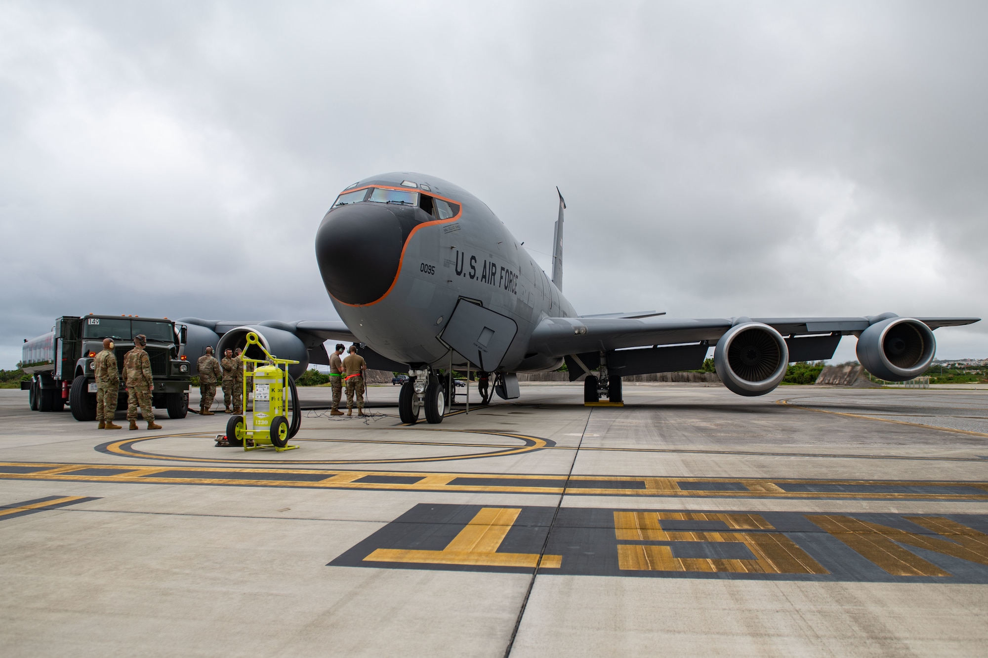 A plane and refueling truck sit side by side as airmen watch the refueling process.