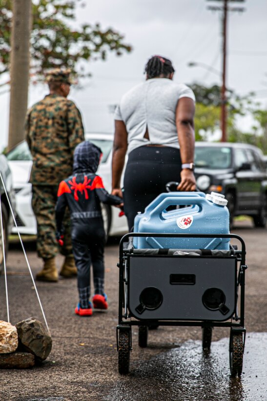 A child helps his mother pick up potable water at a water distribution point, Manana Housing Community, Pearl City, Hawaii, Dec. 14, 2021. U.S. Marines with 3rd MLG, as part of Task Force KULEANA, are providing support services such as drinking water, field expedient showers and laundry facilities to the residents of Joint Base Pearl Harbor-Hickam affected by the ongoing water issue. 3rd MLG, based out of Okinawa, Japan, is a forward deployed combat unit that serves as III Marine Expeditionary Force’s comprehensive logistics and combat service support backbone for operations throughout the Indo-Pacific area of responsibility. (U.S. Marine Corps photo by Sgt. Hailey D. Clay)