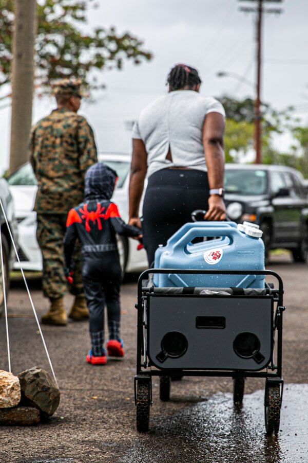 A child helps his mother pick up potable water at a water distribution point, Manana Housing Community, Pearl City, Hawaii, Dec. 14, 2021. U.S. Marines with 3rd MLG, as part of Task Force KULEANA, are providing support services such as drinking water, field expedient showers and laundry facilities to the residents of Joint Base Pearl Harbor-Hickam affected by the ongoing water issue. 3rd MLG, based out of Okinawa, Japan, is a forward deployed combat unit that serves as III Marine Expeditionary Force’s comprehensive logistics and combat service support backbone for operations throughout the Indo-Pacific area of responsibility. (U.S. Marine Corps photo by Sgt. Hailey D. Clay)