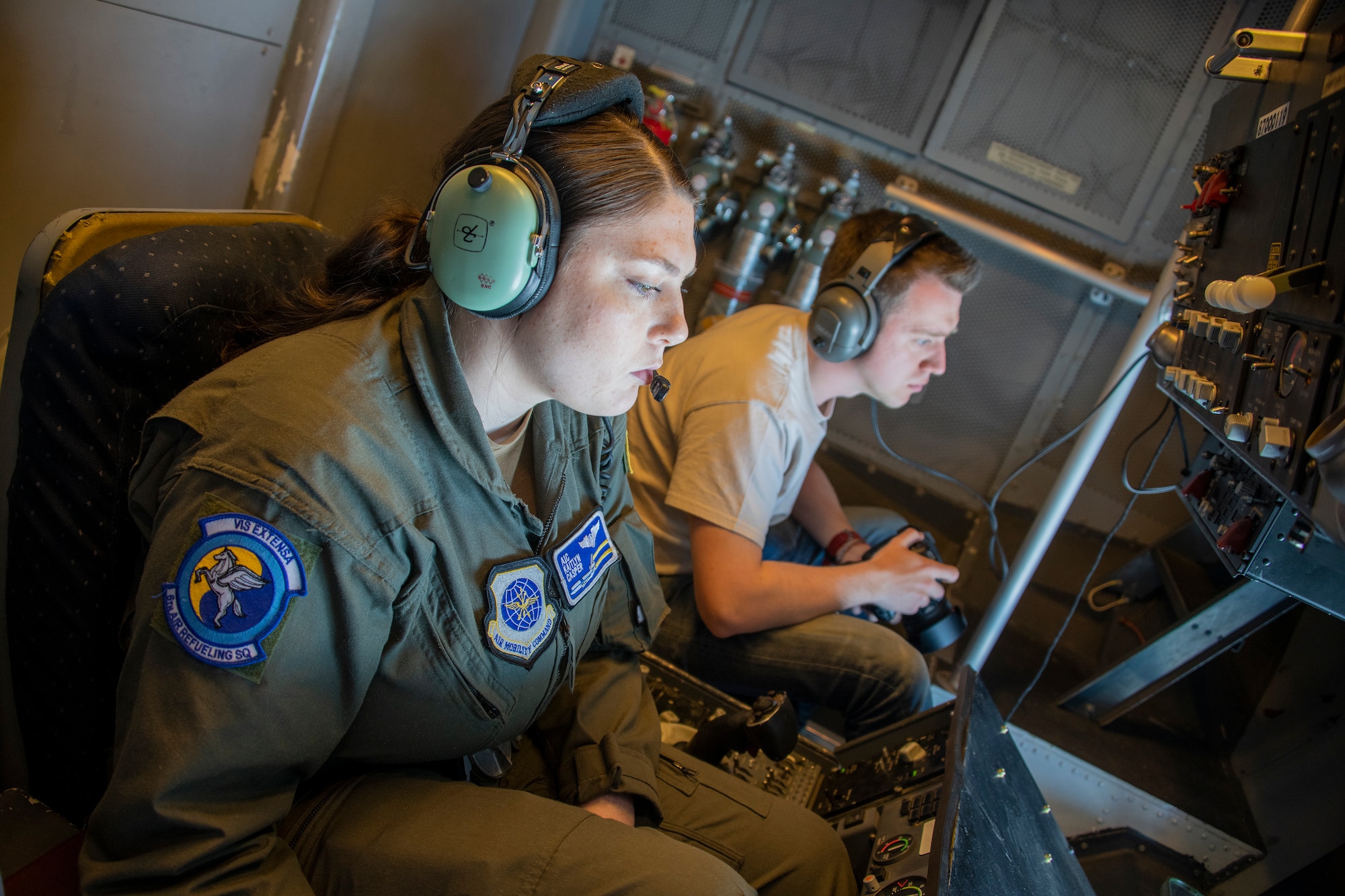 U.S. Air Force Airman 1st Class Kaitlyn Casper, left, 6th Air Refueling Squadron in-flight refueling specialist, waits for an approaching aircraft to maneuver into position to be refueled while aviation photojournalist Matthew Mansell, was on board documenting the operation during the Women’s History Month heritage flight at Travis Air Force Base, California, March 22, 2022.  The remarkable ability of aircraft to be refueled while still in flight depends on the skills of in-flight refueling personnel, more commonly known as boom operators. In honor of Women's History Month, an all-female KC-10 flight crew from the 60th and 349th Air Mobility Wings flew on an aerial refueling training mission over California and Oregon. (U.S. Air Force photo by Heide Couch)