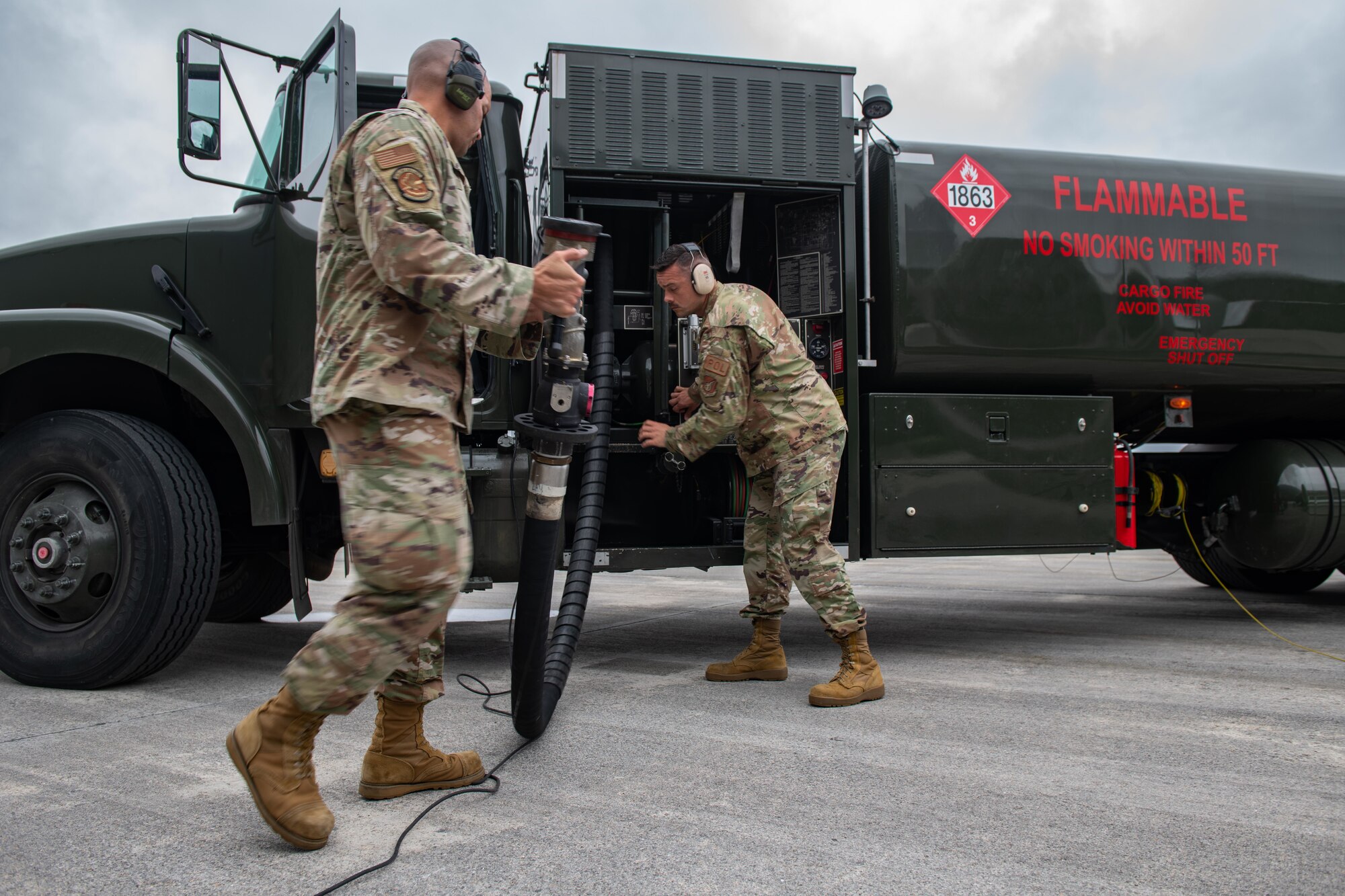 Two airmen roll up a fuel hose into a truck
