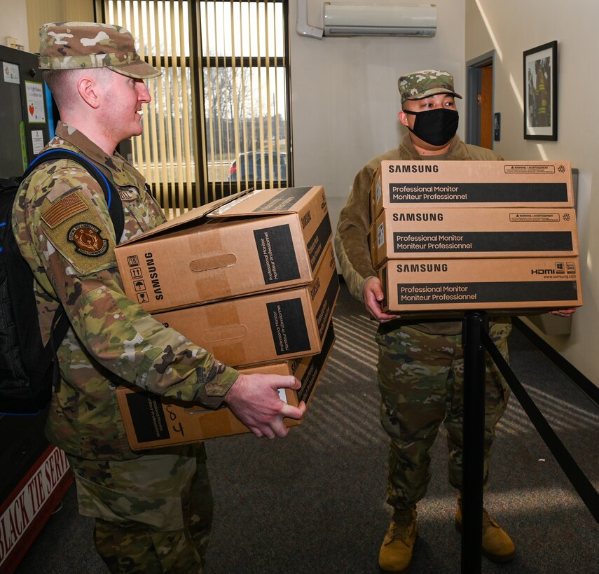 Two males hold a computer monitor