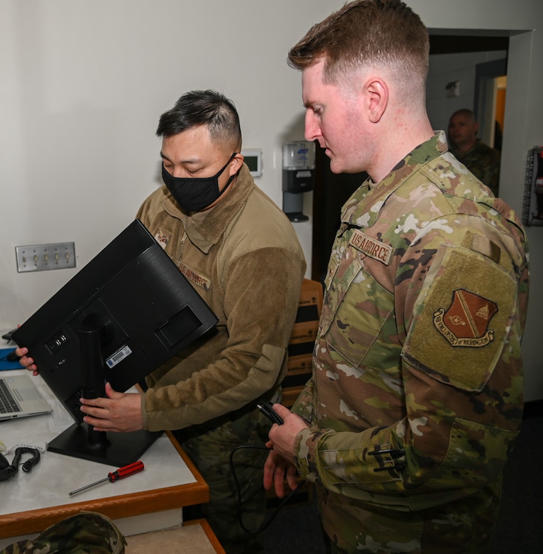 Two males hold a computer monitor
