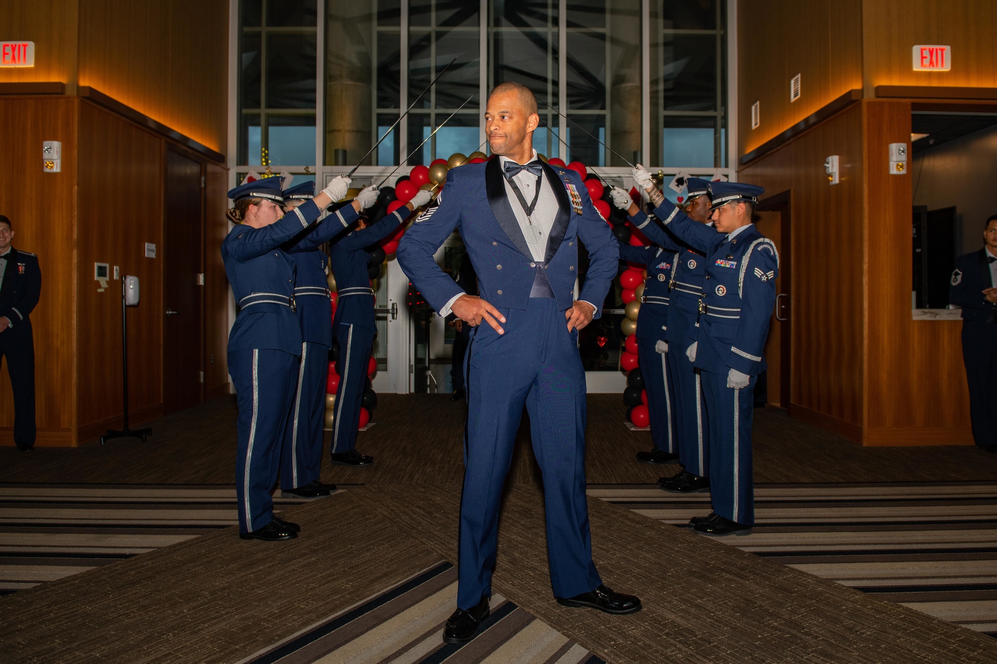 An airman poses heroically in between a row of swords being held by the honor guard