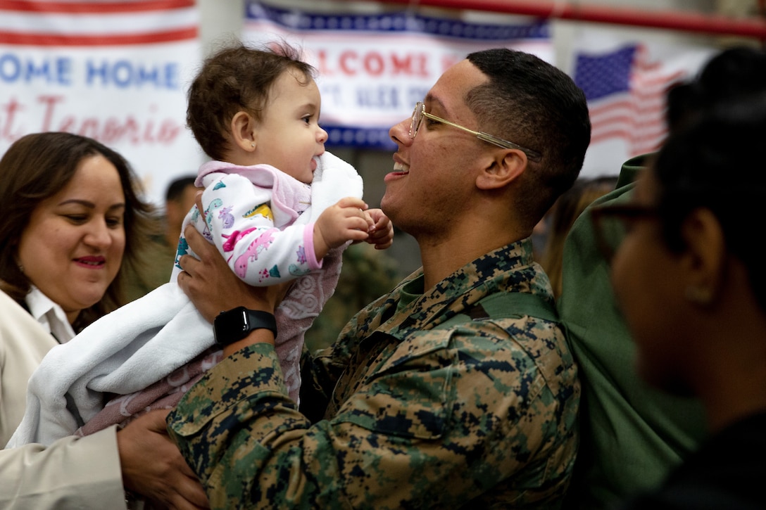 A Marine smiles as he holds a young girl.