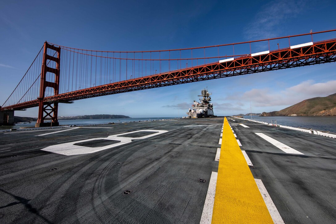 A large ship steams under a bridge.