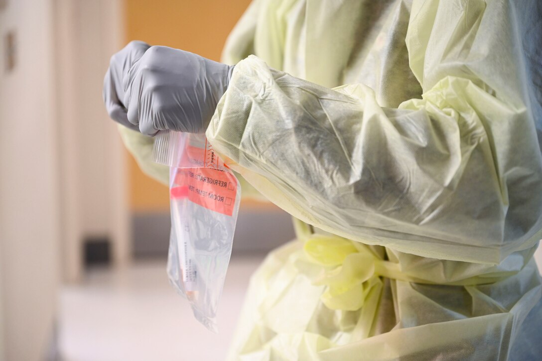 An airman wearing protective gear seals a bag with a COVID-19 nasal swab.