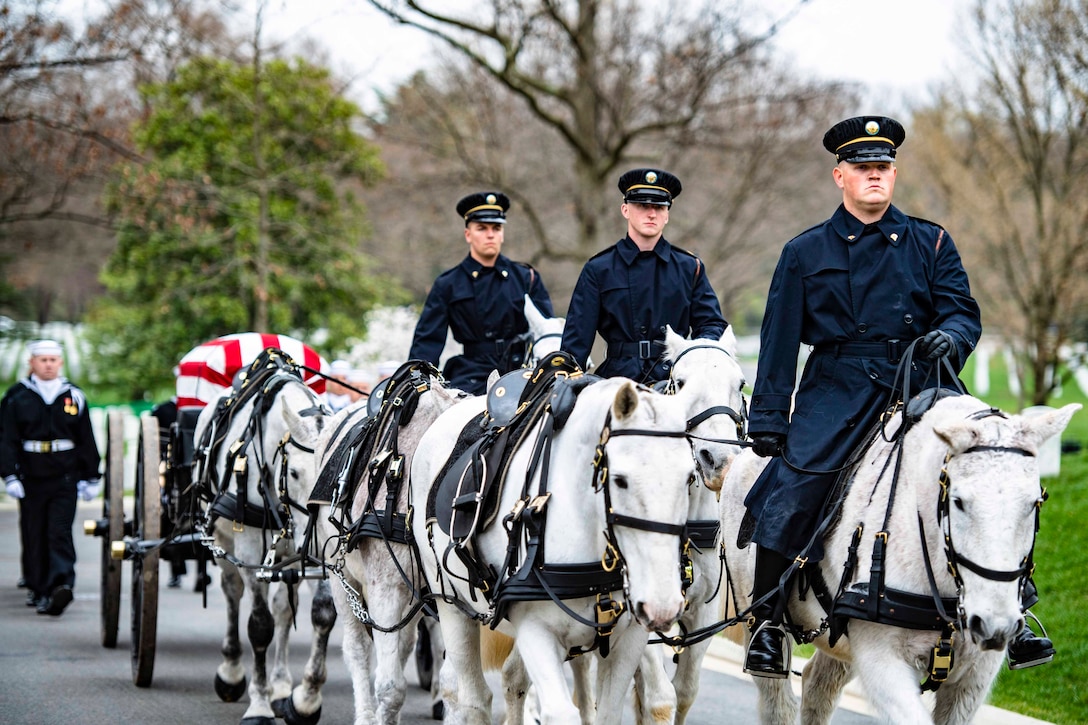 Soldiers ride on horses as a carriage carries a casket behind.