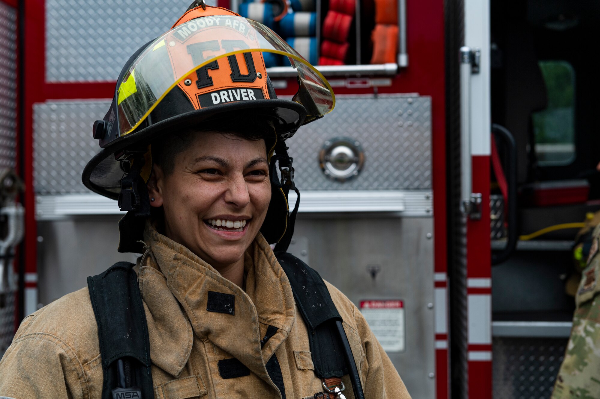 Photo of an Airman smiling while trying on firefighter equipment
