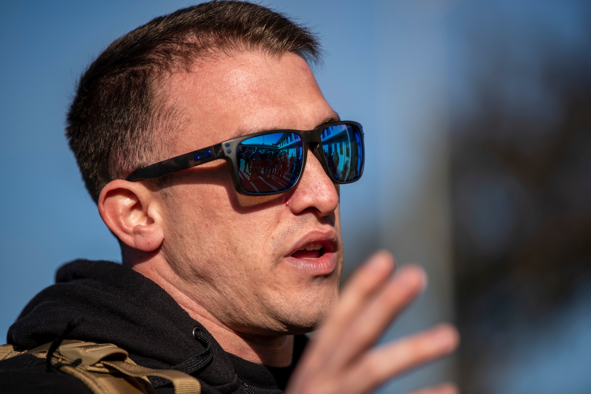 An Airman wearing black rimmed sun glasses is seen talking. The picture was taken very close to him so his head fills the frame.