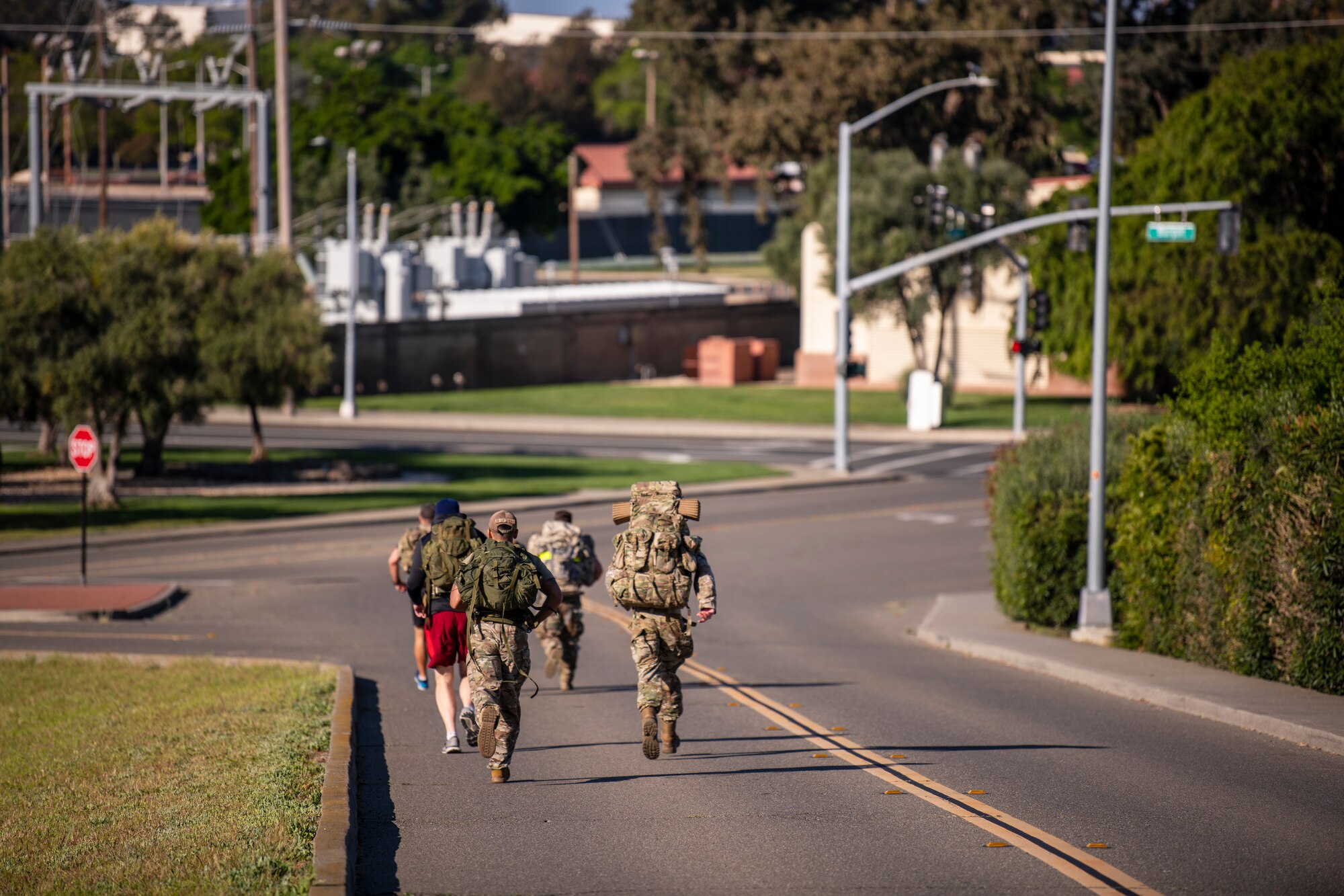 Service members are seen running down a road all wearing large ruck sacks on their backs.