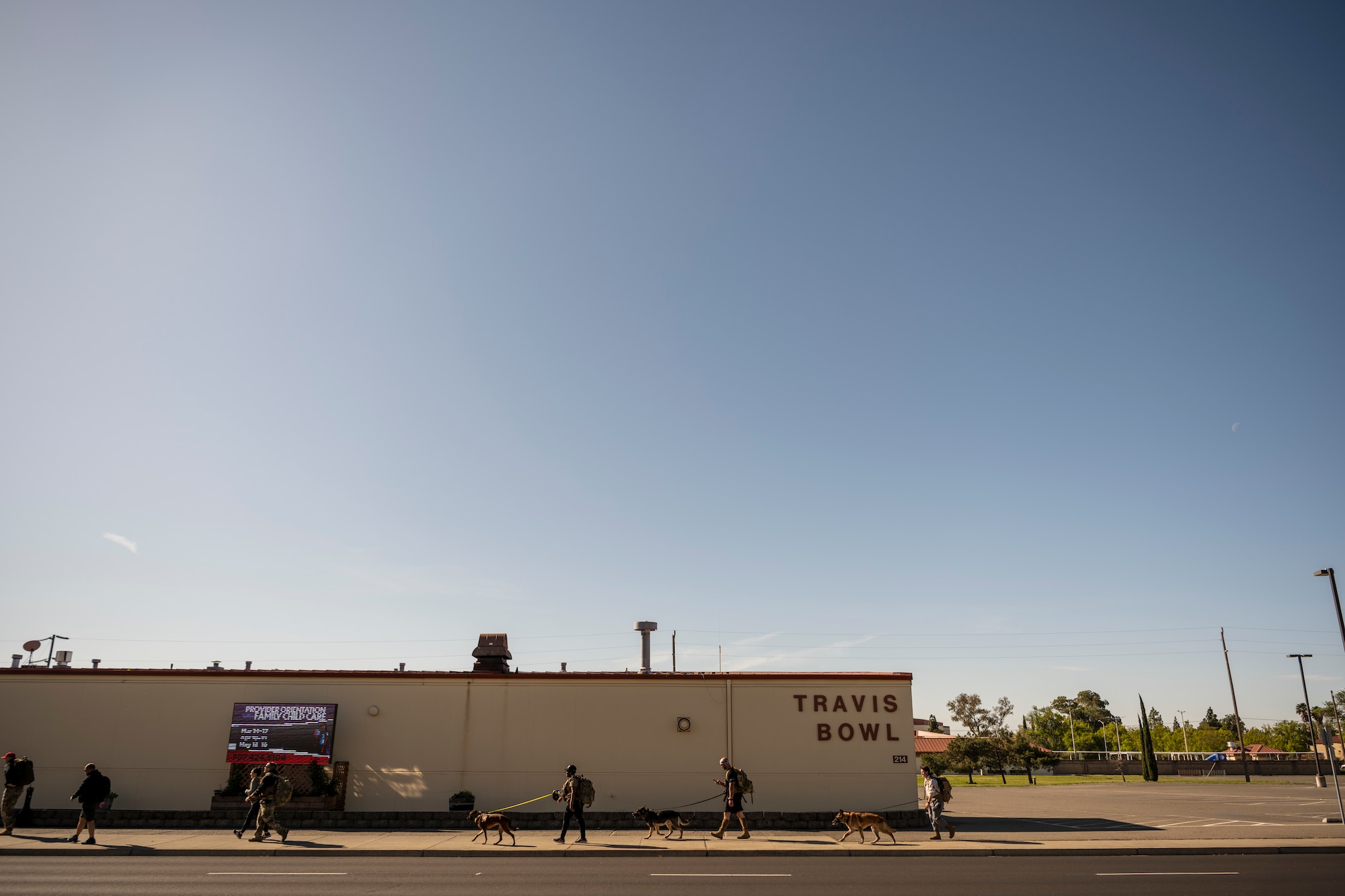 Service members walk along a sidewalk in front of a large building that reads "Travis Bowl."