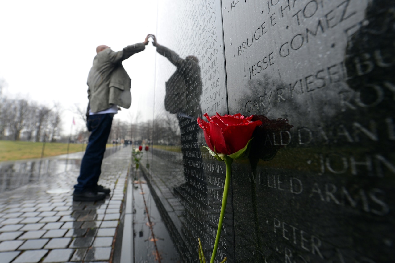 A person with raised arm is reflected while touching a wall.