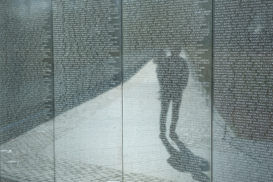 A person's reflection is seen standing in front of the Vietnam Veterans Memorial wall.