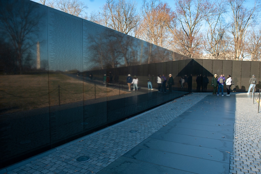 A group of people look at the names on the Vietnam Veterans Memorial wall.