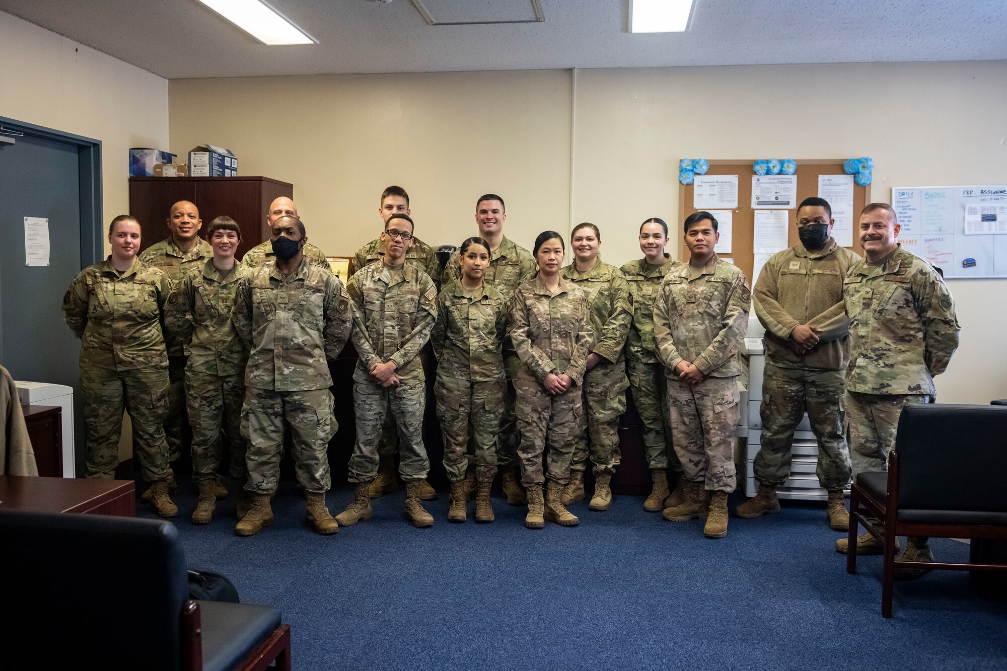 Military members in uniform pose for a group photo in an office.