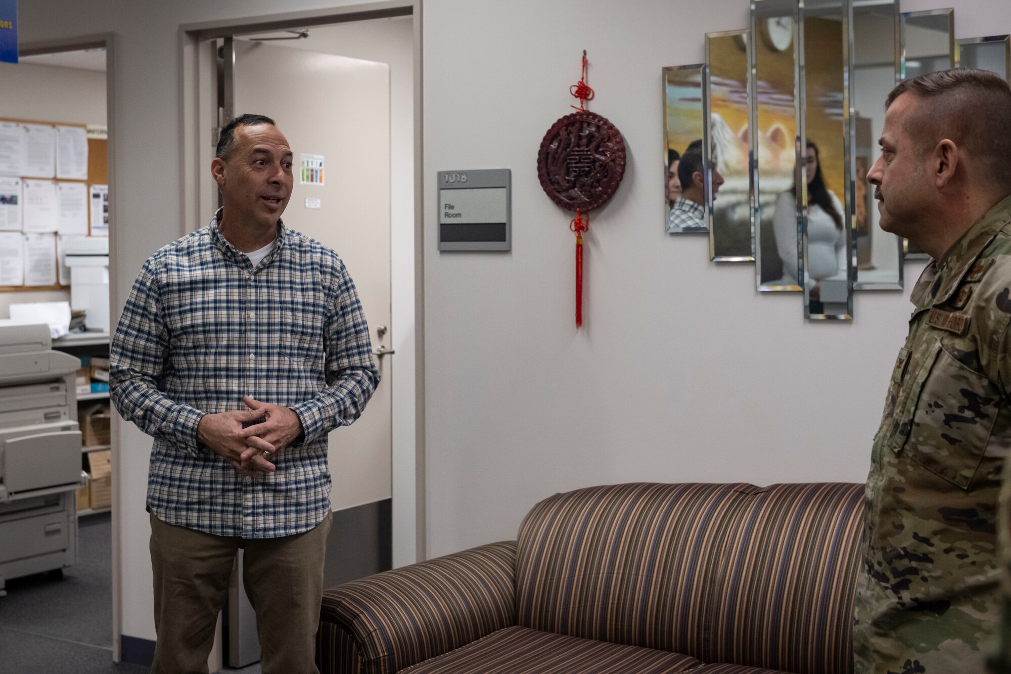 A military member in uniform talks with civilians in an office.