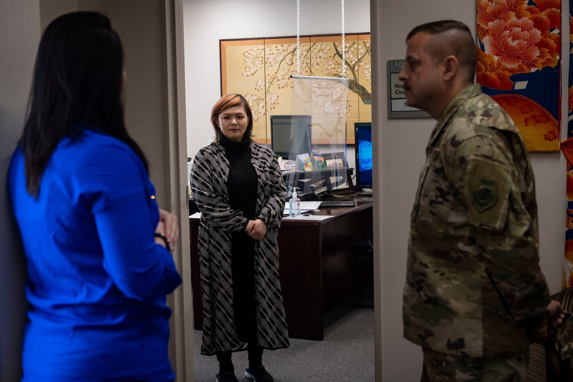 A military member in uniform talks with civilians in an office.