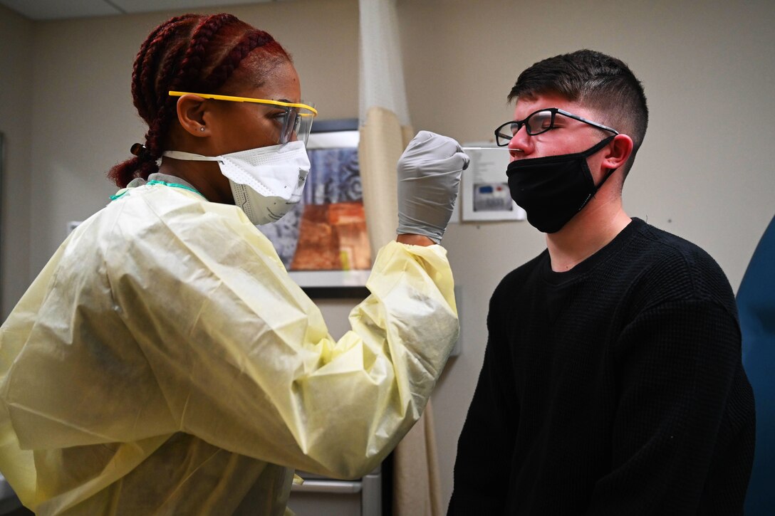 An airman wearing a face mask, gloves and medical gown performs a COVID-19 test on a patient.