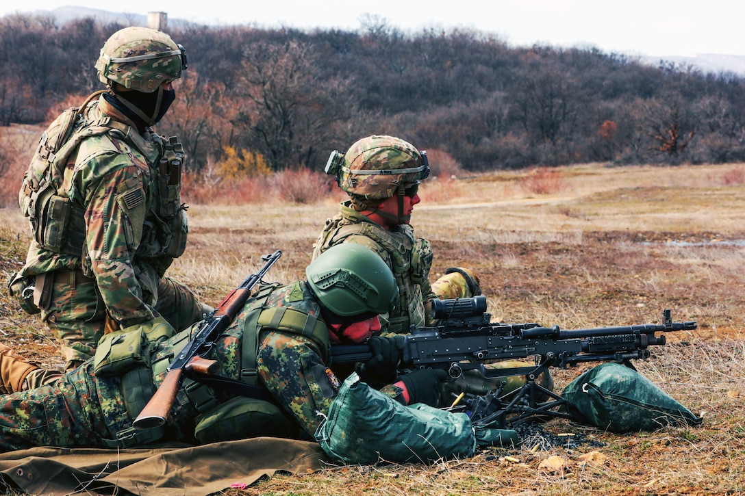 Two soldiers train a member of the Bulgarian land forces to use a machine gun.