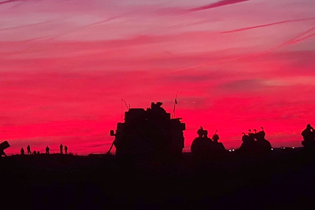 Soldiers and vehicles are silhouetted against a red sky.