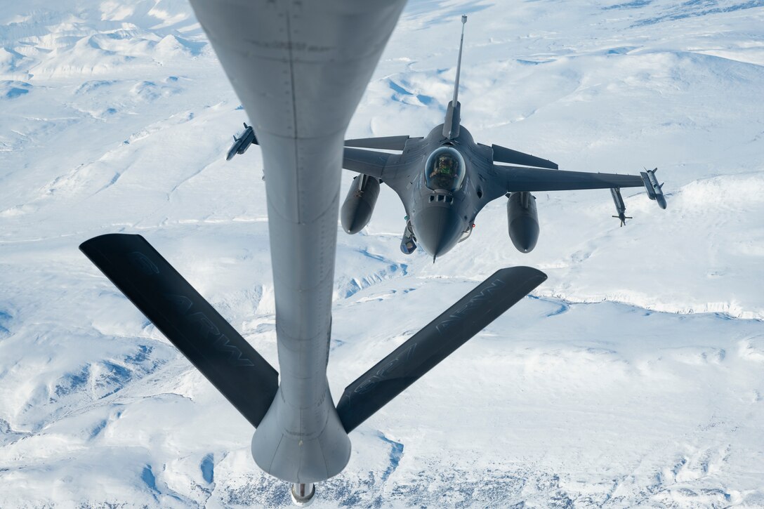 A fighter jet flies above an icy landscape.