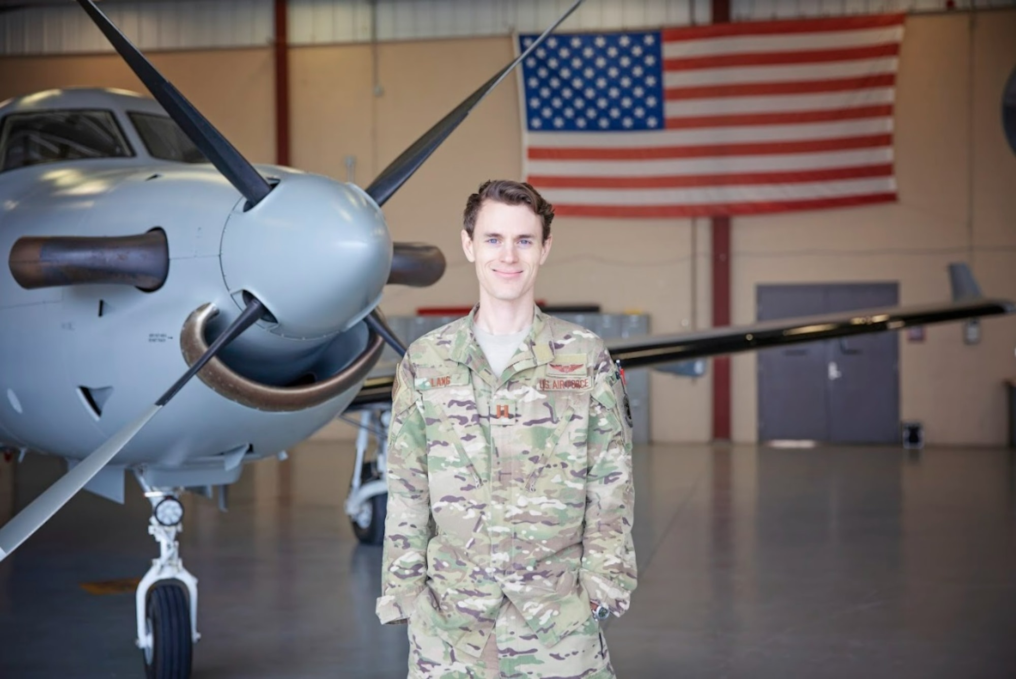 An officer stands in front of an aircraft inside of a hangar.
