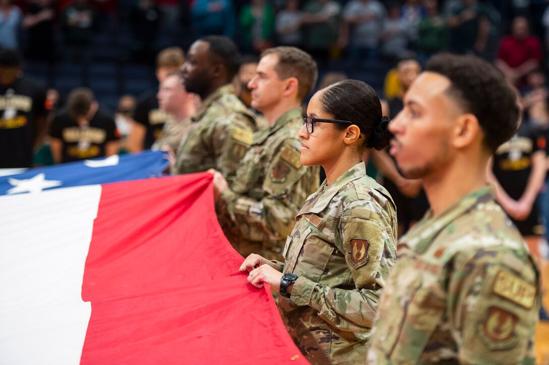 Airmen hold an American flag during basketball game.