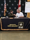 woman in U.S. Army uniform shakes hands with a man in a white shirt, sitting behind a table.