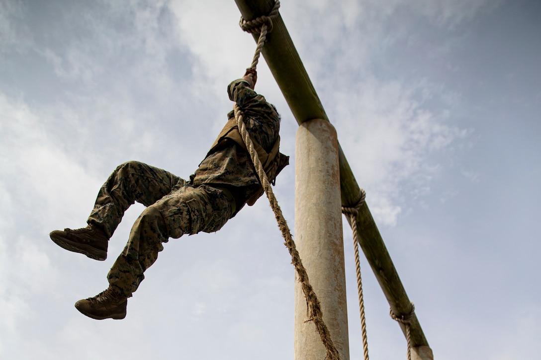 A Marine climbs up a rope during a course.