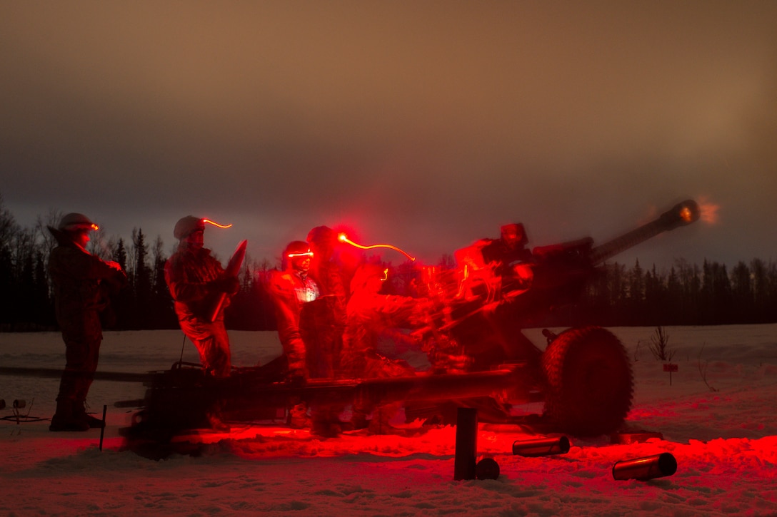 Soldiers fire a weapon in the dark illuminated by red lights.