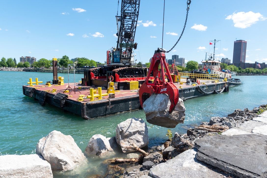 A crane barge lifts a large stone.
