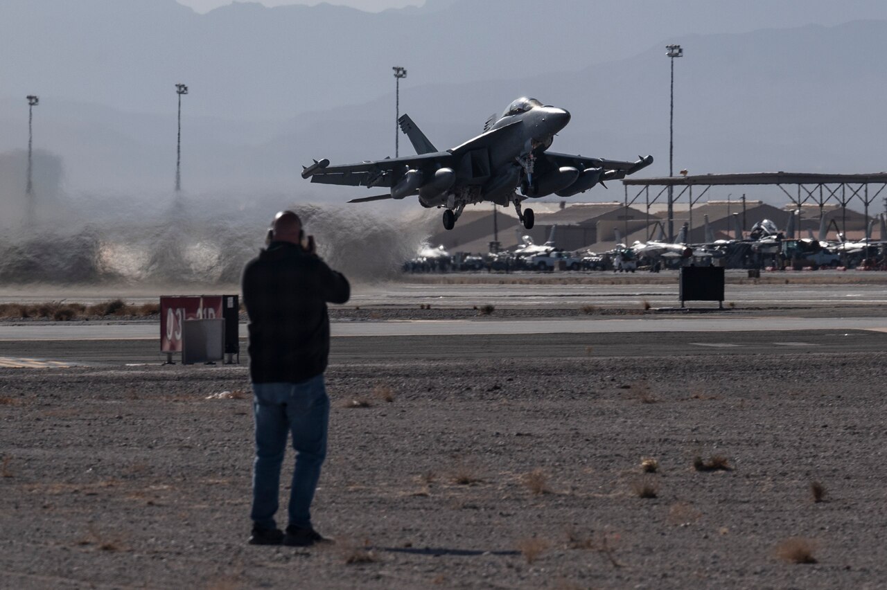 An aircraft lifts off a runway in a desert environment.