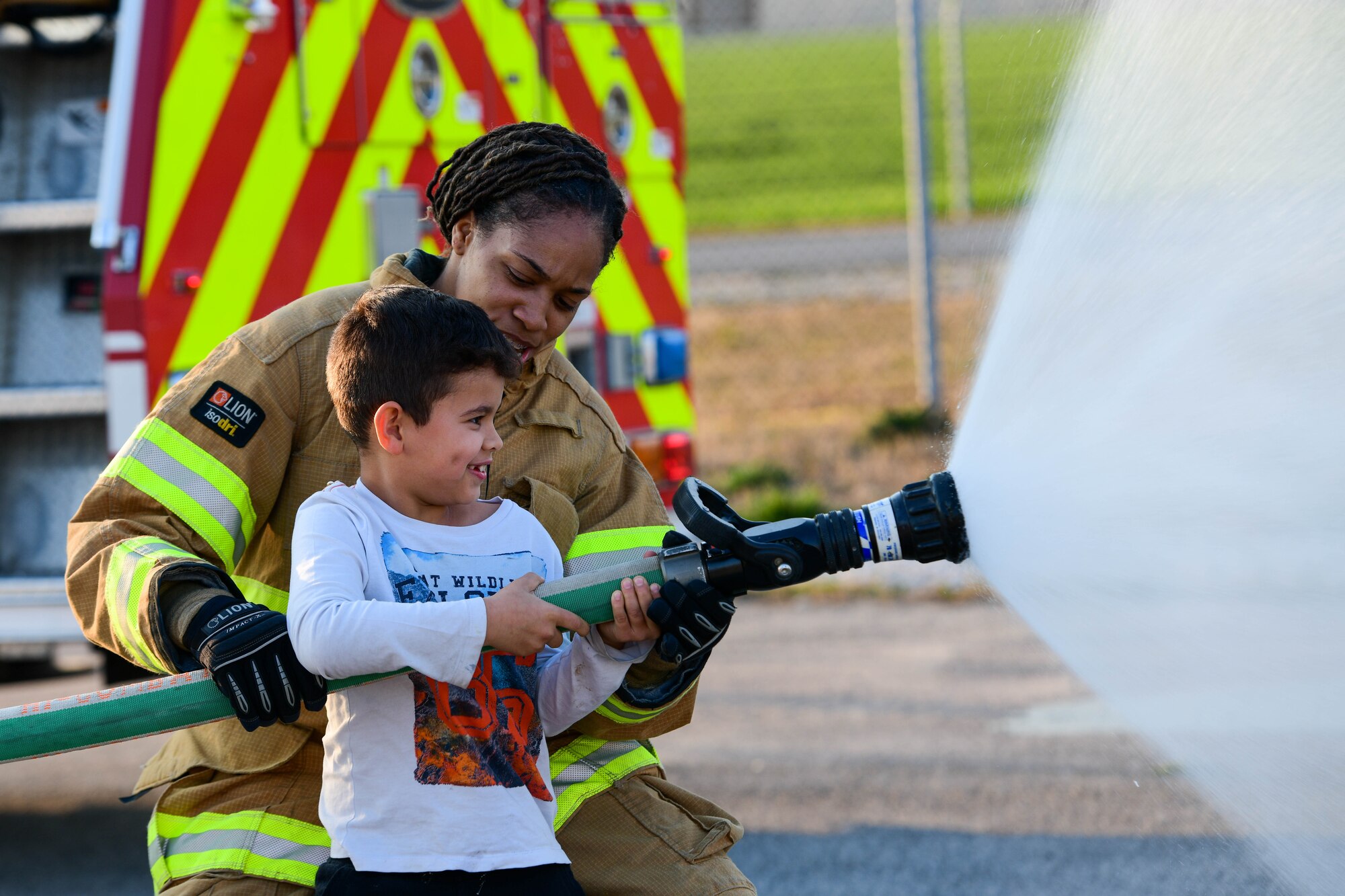 Senior Airman Kayla Jerido, 31st Civil Engineer Squadron Fire Department firefighter, helps a child spray a fire hose during a 31st CES immersion at Aviano Air Base, Italy, March 24, 2022. U.S. Air Force Airmen in different 31st CES sections held an immersion with Wyvern families to showcase their operations, including a live burn demonstration. (U.S. Air Force photo by Senior Airman Brooke Moeder)