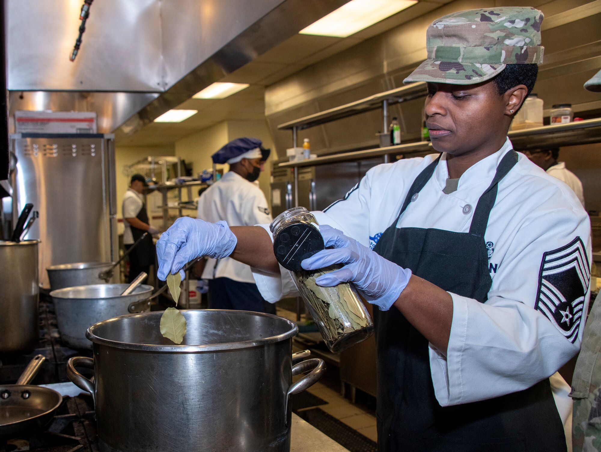 U.S. Air Force Chief Master Sgt. Andrea Conlan, 60th Force Support Squadron senior enlisted leader, adds bay leaves to flavor a dish at Travis Air Force Base, California, March 23, 2022. The 60th Mission Support Group Monarch Dining Facility hosted a cooking competition showcasing skill, speed and ingenuity. Teams of four competed to transform mystery ingredients into the main course and dessert dishes to present to a panel of judges. (U.S. Air Force photo by Heide Couch)