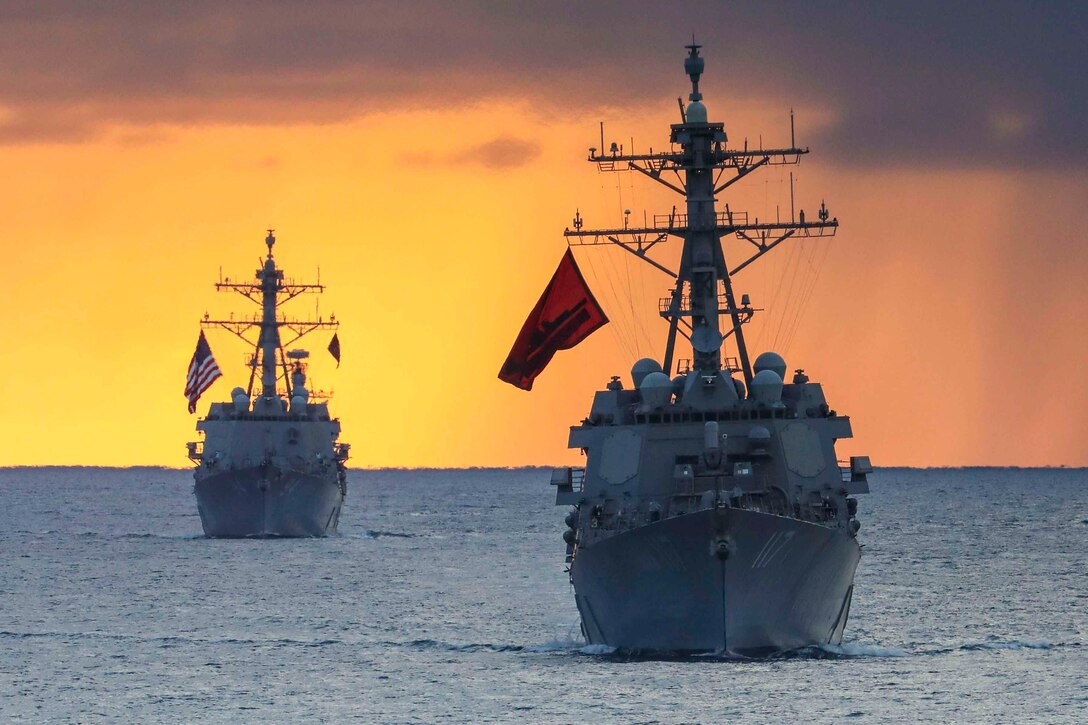 Two ships sail in formation through waters.