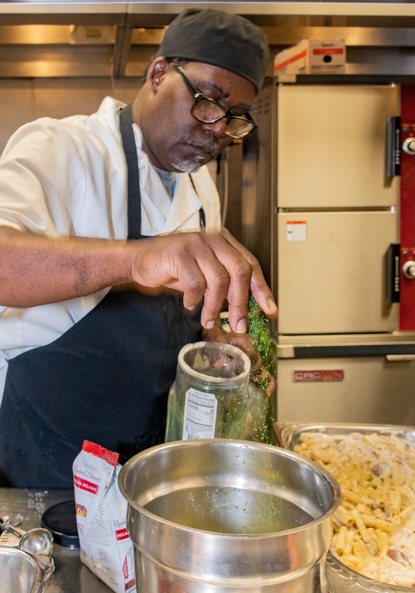 Reginald Barkus, 60th Force Support Squadron food service cook, adds parsley to a mixing bowl at Travis Air Force Base, California, March 23, 2022. The 60th Mission Support Group Monarch Dining Facility hosted a cooking competition showcasing skill, speed and ingenuity. Teams of four competed to transform mystery ingredients into the main course and dessert dishes to present to a panel of judges. (U.S. Air Force photo by Heide Couch)