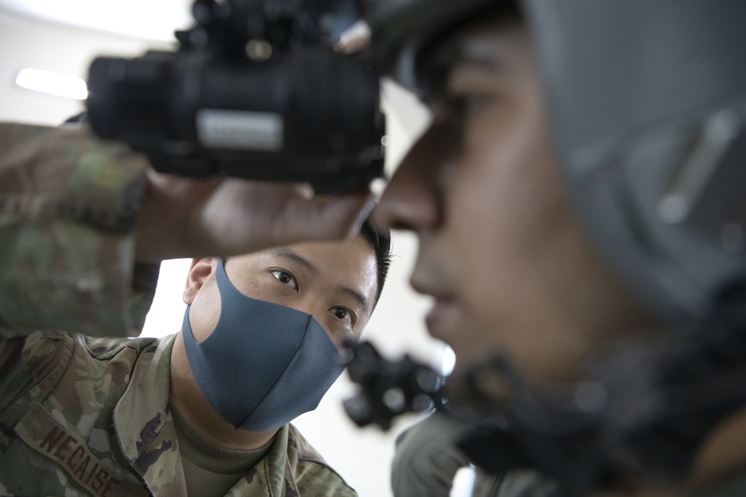 An airman helps another airman with his goggles.