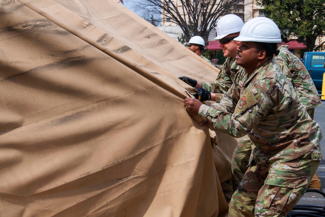 Airmen pull off the former COVID-19 testing tent rain cover during its dismantling at Yokota Air Base.