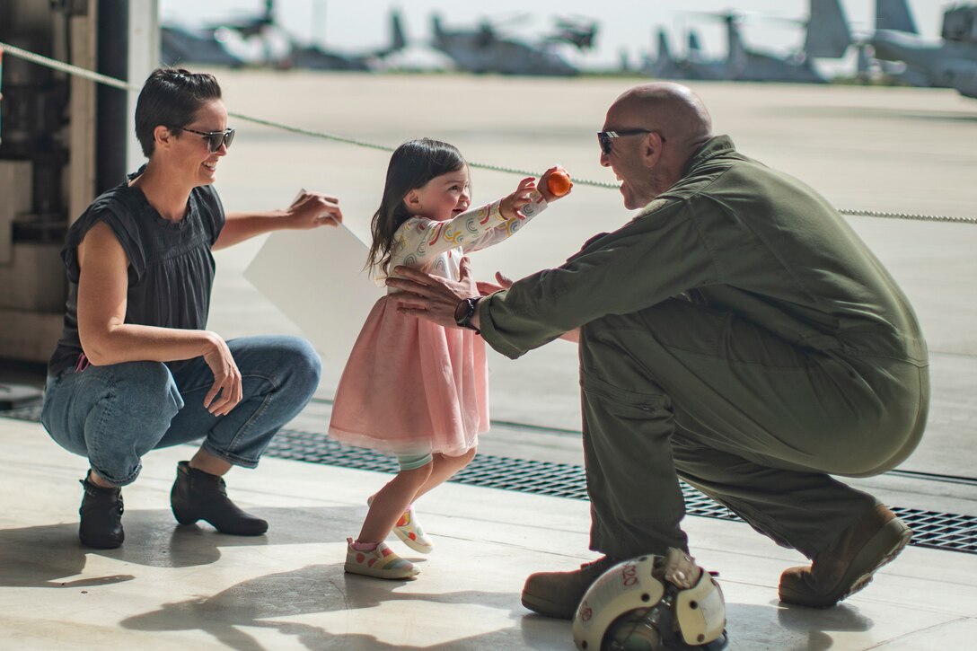 A Marine kneels and holds his daughter as she runs up to him.