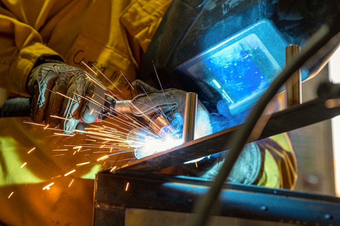 An airman wearing protective gear welds sheet metal.